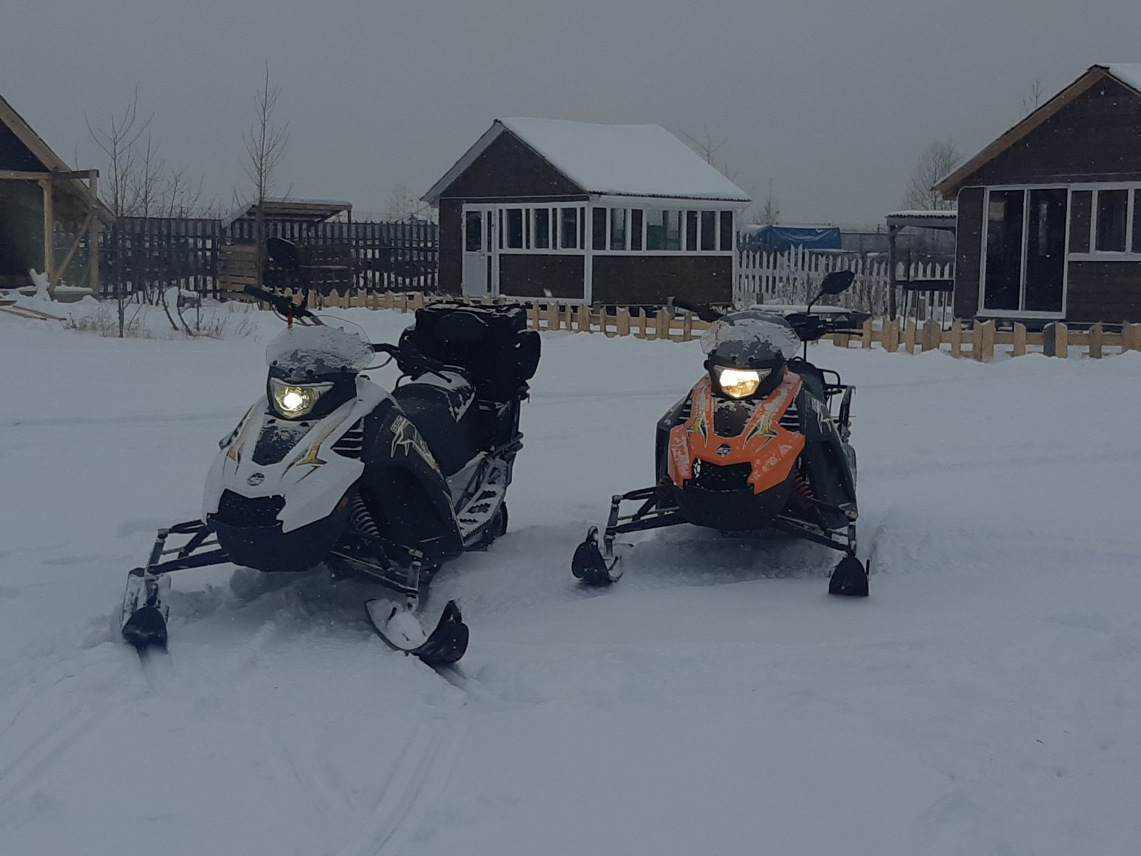 Безопасное катание на снегоходе по зимней трассе. Фото двух людей в зимней спецодежде и снегоходном шлеме во время езды на снегоходе